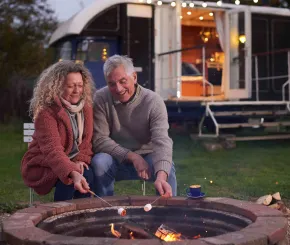A couple sitting happily around a camp fire with coffee and holiday home