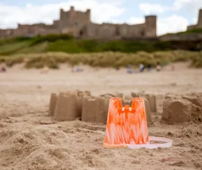 A sandcastle on the beach in the foreground, with an actual castle in the background
