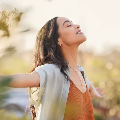 image of a woman at peace in an idyllic scene outdoors in nature standing with arms spread wide with a sense of freedom