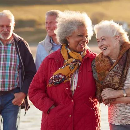 image of windswept elderly individuals walking arm in arm along a beach